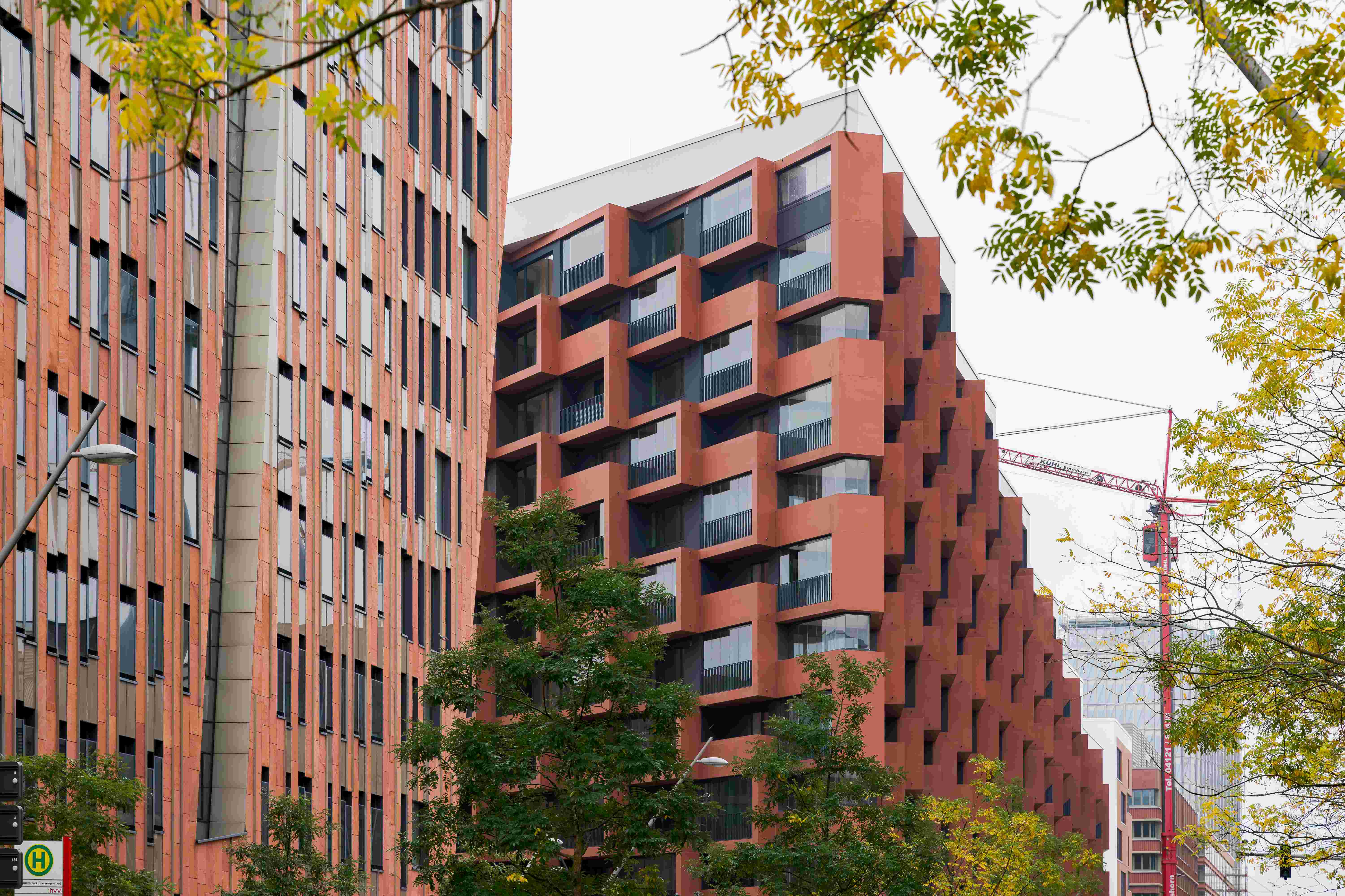 Wohngebäude „Eleven Decks“ in der HafenCity Hamburg mit roten Fassaden, großen Fenstern und geometrischen Balkonen, umgeben von Herbstbäumen.