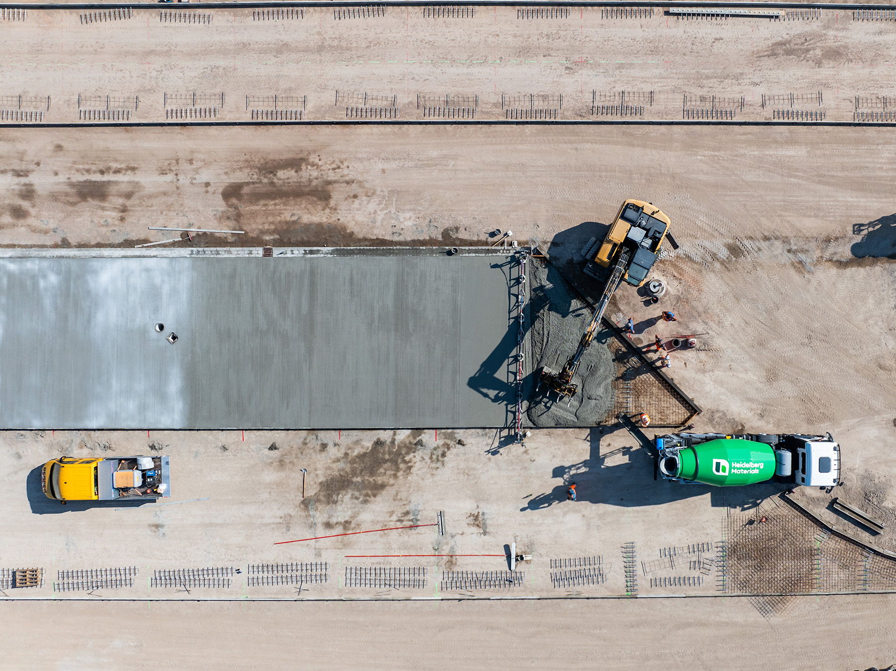 Luftaufnahme einer Baustelle mit einer frisch gegossenen Betonplatte. Daneben der grüne Fahrmischer von Heidelberg Materials.