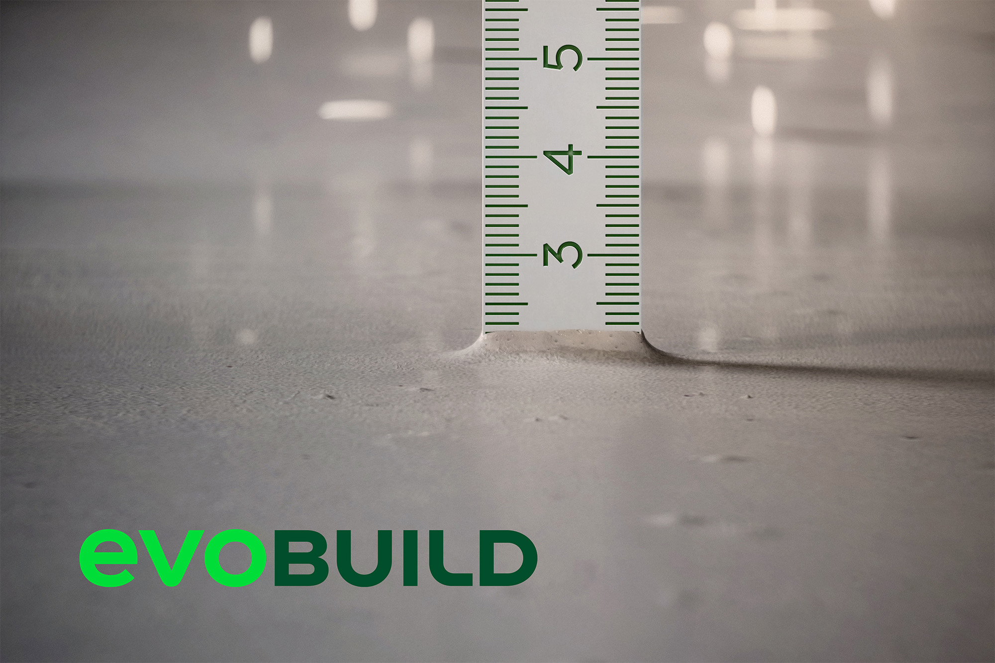 Nahaufnahme eines Zollstocks, der die Tiefe der Bodenoberfläche anzeigt. Unten links das grüne Logo von "evoBuild".