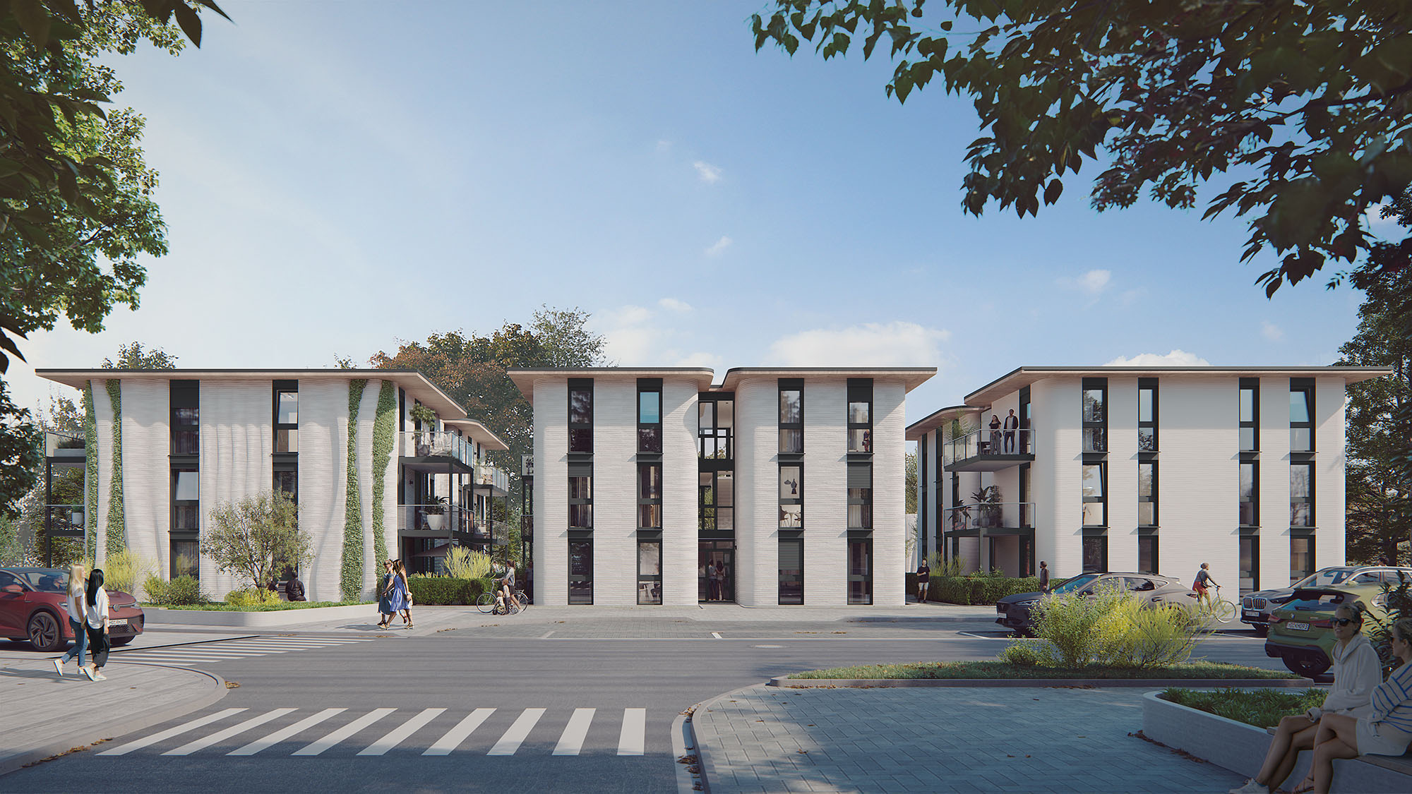 Moderne Wohnanlage mit drei weißen, mehrstöckigen Gebäuden, großen Fensterfronten und einigen vertikalen Begrünungen. Im Vordergrund ein Zebrastreifen, geparkte Autos und Gehwege, umgeben von Bäumen und Grünflächen. Blauer Himmel im Hintergrund.