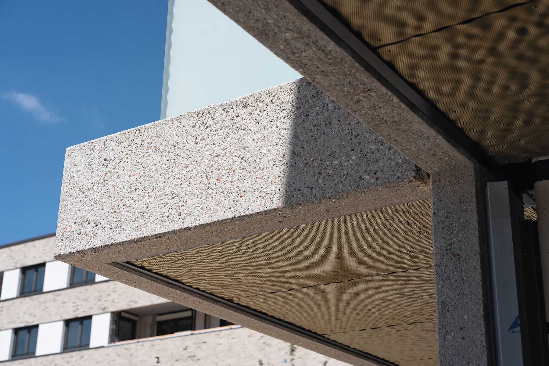 Detailaufnahme eines horizontalen Sichtbetonvorsprungs aus gestocktem RC-Beton mit sichtbaren Zuschlägen und Schattenwurf.