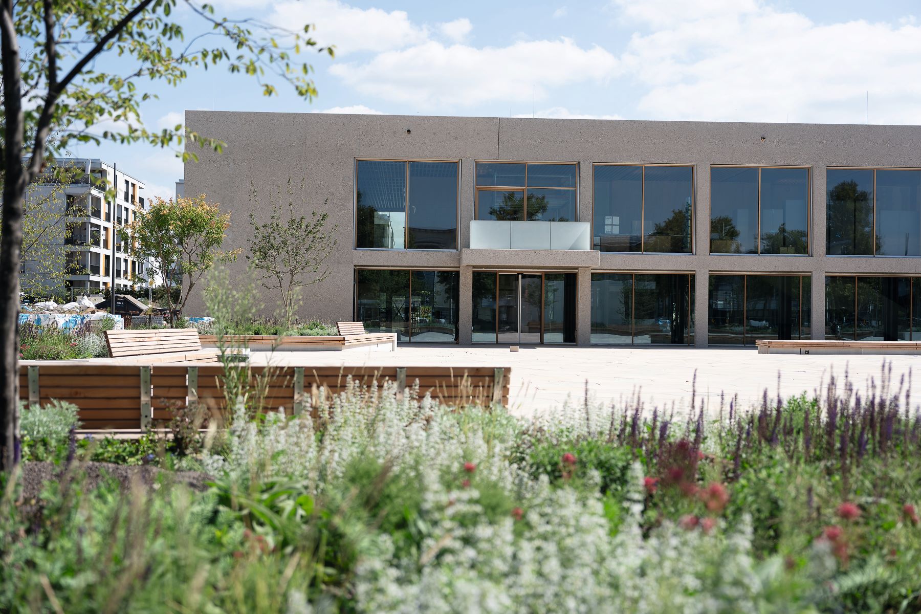 Frontansicht des zweigeschossigen Bürgerhauses mit großen Fensterflächen, vorgelagerter Platzgestaltung und bepflanzten Aufenthaltsbereichen.