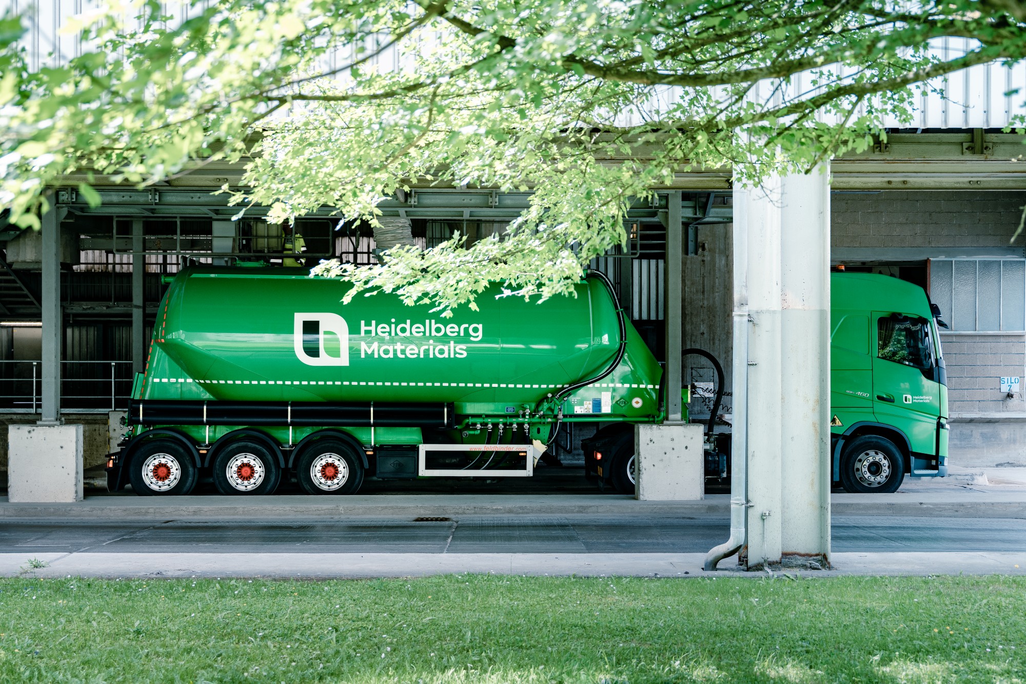 Ein grünes Silofahrzeug mit Heidelberg Materials-Logo steht auf einem Industriegelände.