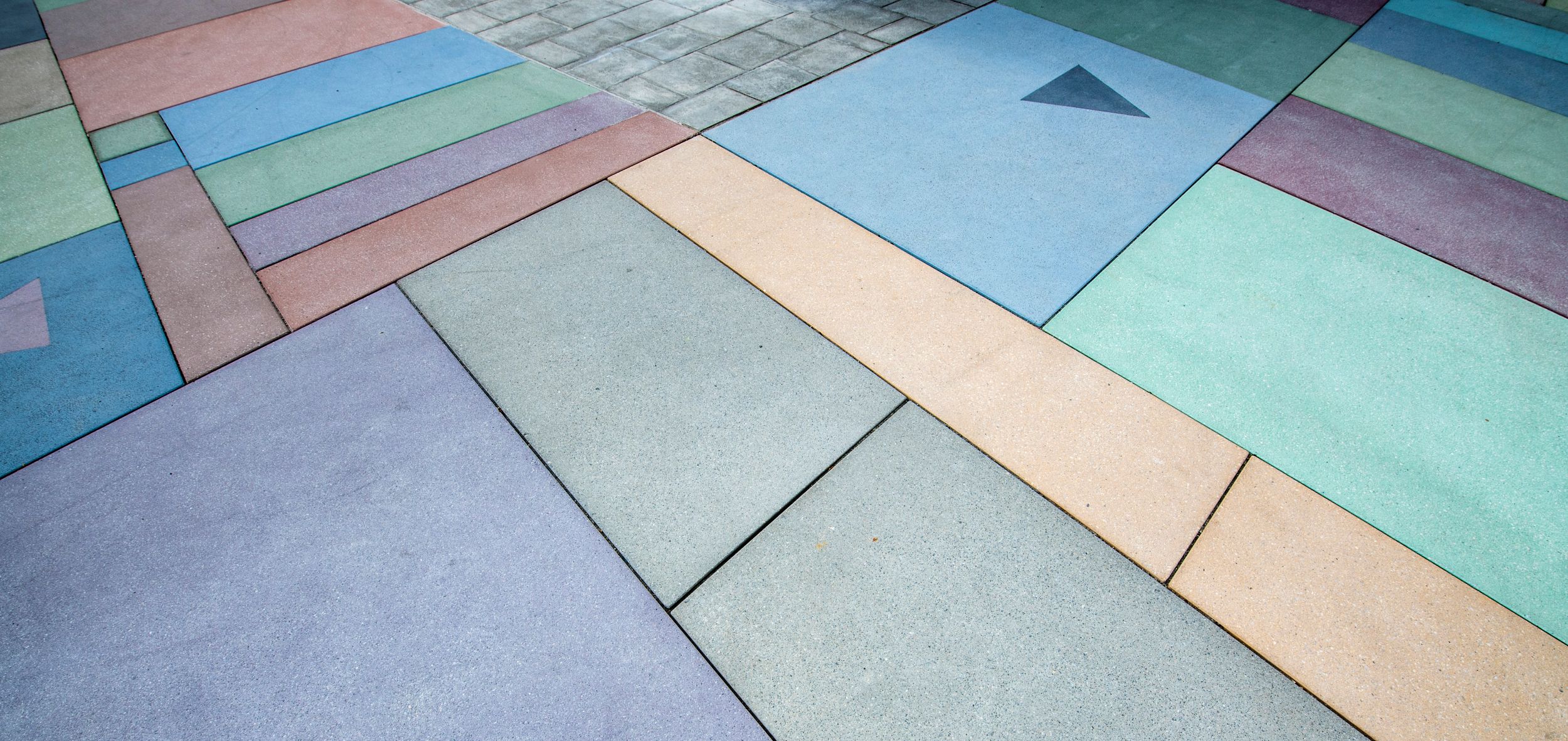 Farbig gestaltete Betonplatten in geometrischen Mustern auf einer Bodenfläche.