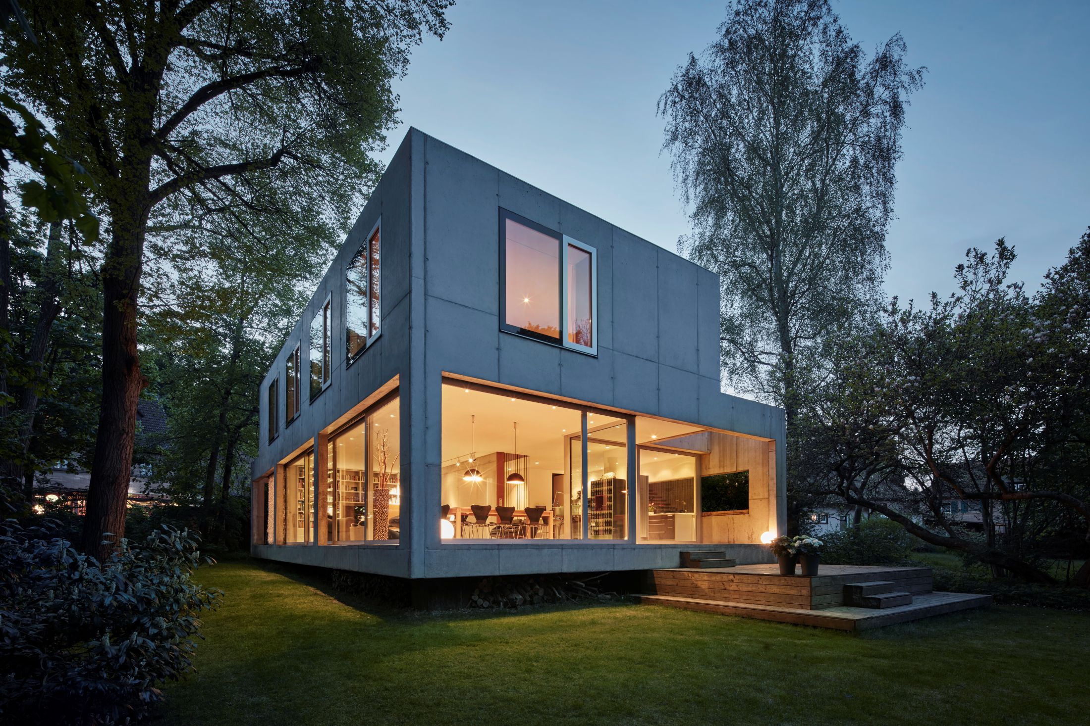 Modernes Gebäude aus Beton mit großen Glasflächen, umgeben von einer Gartenlandschaft.