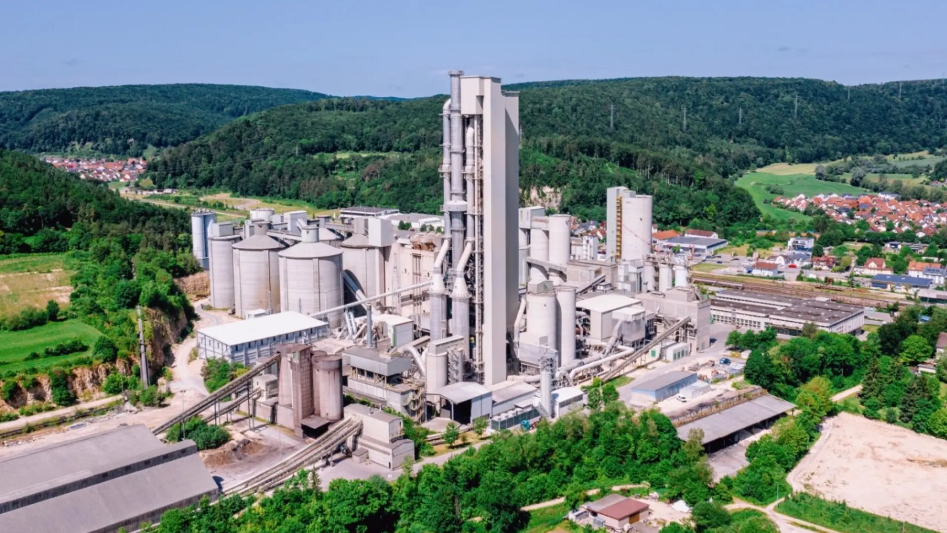 Industriegelände mit Zementwerk, umgeben von grüner Landschaft und Hügeln.
