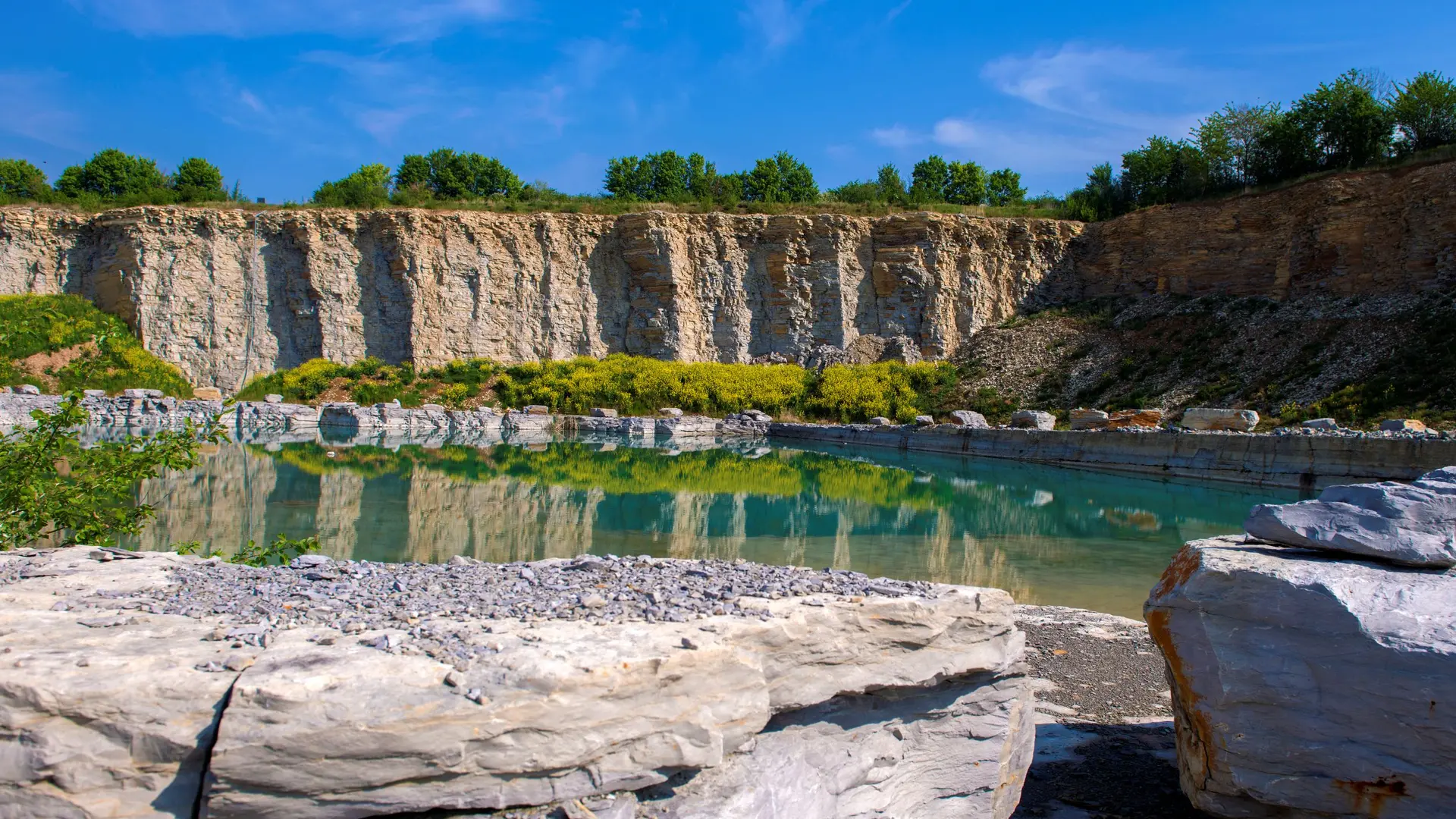 Steinbruch Geseke mit Wasser, umgeben von steilen Felswänden und grüner Vegetation.