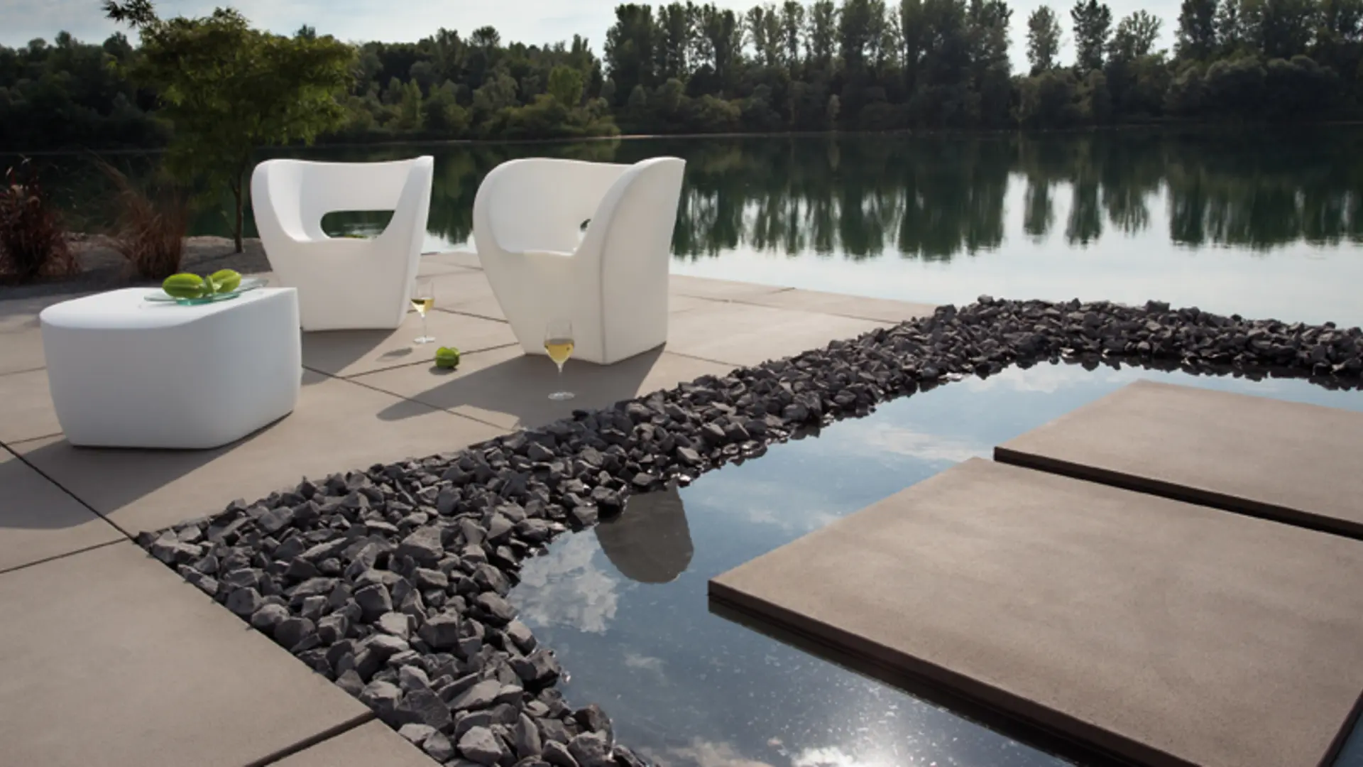 Terrasse mit modernen Betonplatten am Wasser, umgeben von Natur.