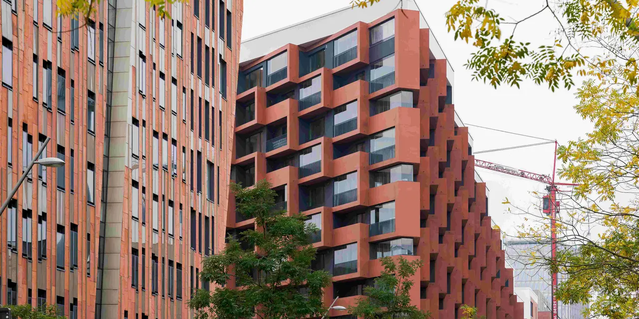 Wohngebäude „Eleven Decks“ in der HafenCity Hamburg mit roten Fassaden, großen Fenstern und geometrischen Balkonen, umgeben von Herbstbäumen.