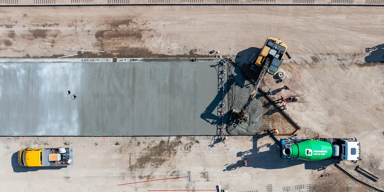 Luftaufnahme einer Baustelle mit einer frisch gegossenen Betonplatte. Daneben der grüne Fahrmischer von Heidelberg Materials.