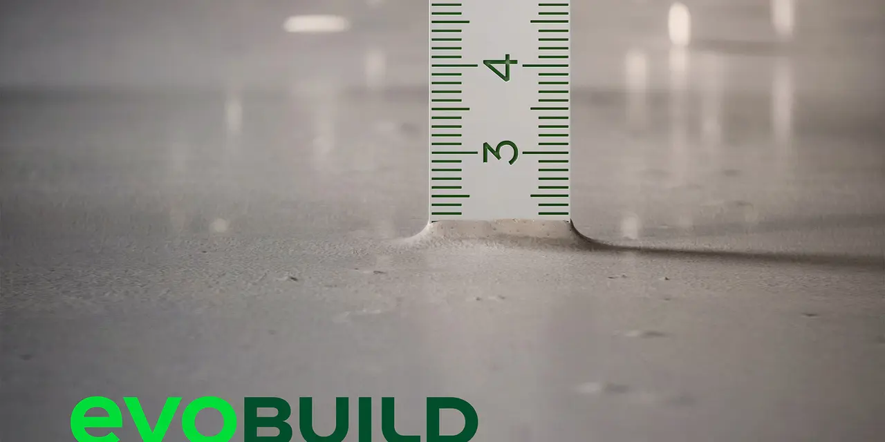 Nahaufnahme eines Zollstocks, der die Tiefe der Bodenoberfläche anzeigt. Unten links das grüne Logo von "evoBuild".
