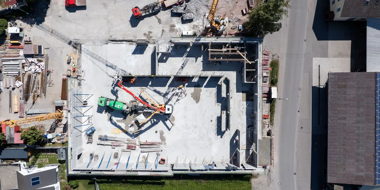 Baustelle mit Betonfundament und Baumaschinen, dargestellt aus der Vogelperspektive.