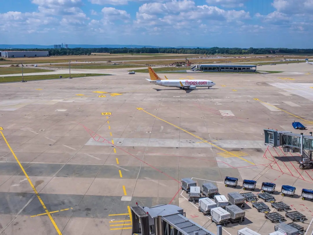 Flugzeug auf einer Rollbahn eines Flughafens mit abgestellten Gepäckcontainern im Vordergrund.