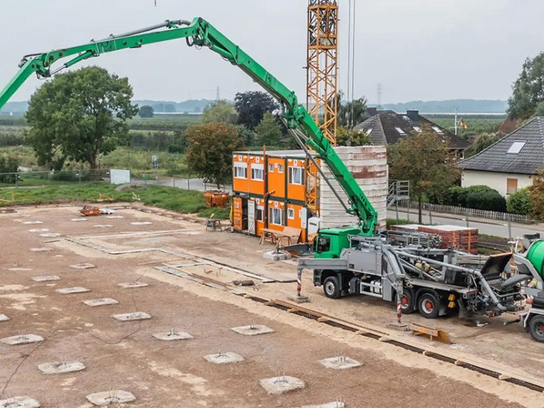 Ein Betonmischer und eine Betonpumpe im Einsatz auf einer Baustelle in ländlicher Umgebung.