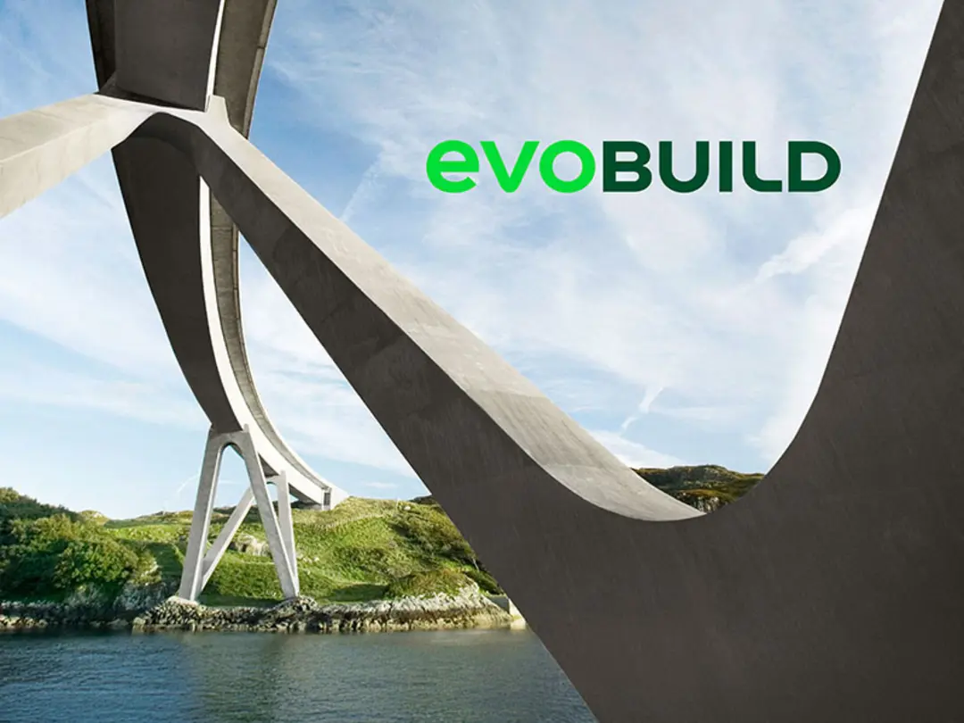 Untersicht einer modernen Brückenkonstruktion mit geschwungenen Betonpfeilern, die eine Flusslandschaft mit grünen Hügeln im Hintergrund überspannt. Oben rechts das Logo „evoBuild“ in grüner und schwarzer Schrift.