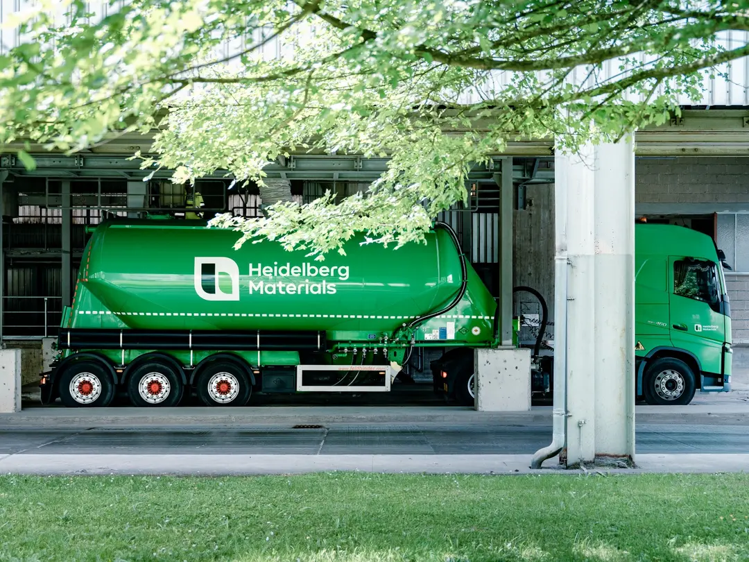 Ein grünes Silofahrzeug mit Heidelberg Materials-Logo steht auf einem Industriegelände.