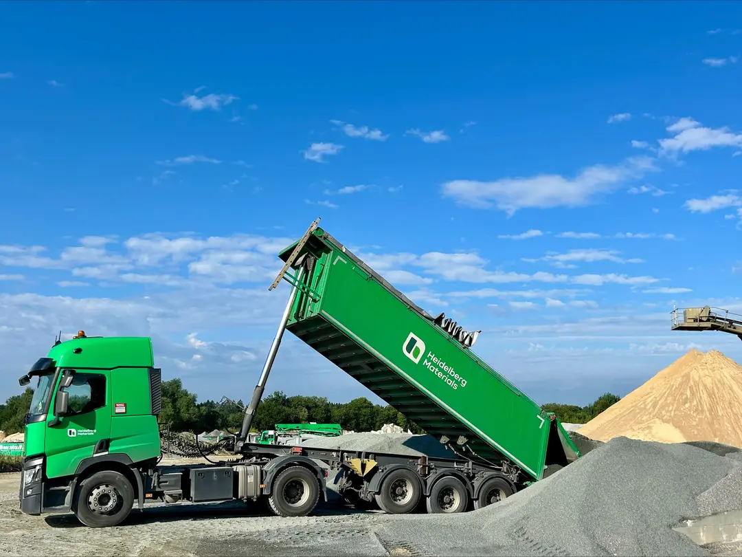 Green truck unloading gravel at a construction site under a blue sky.