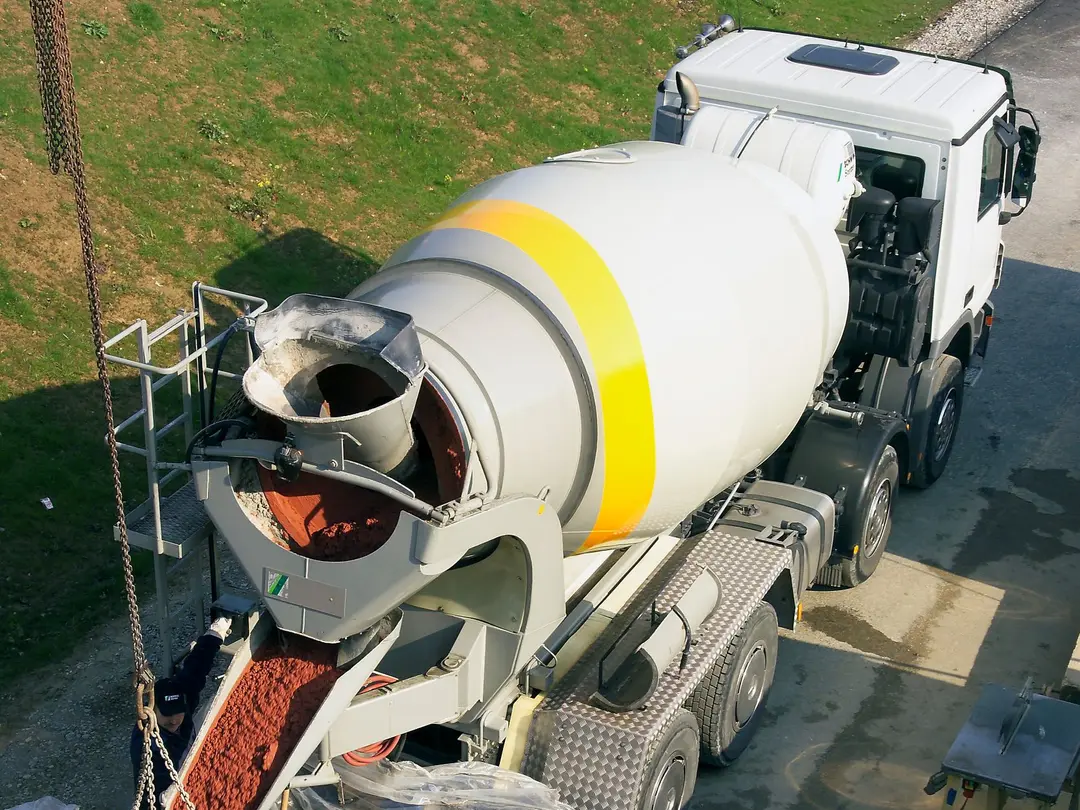 Ein Betonmischfahrzeug entlädt frischen Beton in einen Trichter auf einer Baustelle.