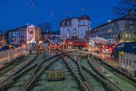 Baustelle bei Nacht mit Baustellenfahrzeugen und Arbeitern an Straßenbahngleisen.