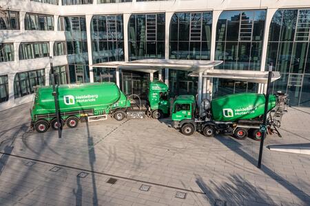 Grüne Fahrzeuge von Heidelberg Materials vor einem modernen Firmengebäude.