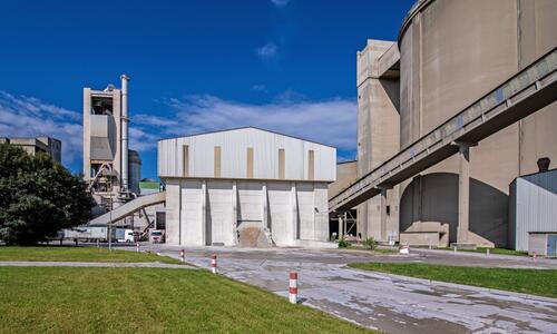 Nach der Zerkleinerung im Brecher zu maximal faustgroßen Schotterstücken wird das Rohmaterial in einer Halle in zwei unterschiedlichen Qualitätsstufen gelagert und von dort im richtigen Mischungsverhältnis einer Rohmühle zugeführt.