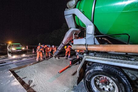 Beton wird bei Nacht aus einem Fahrmischer auf eine Baustelle gegossen.