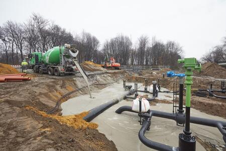 TerraFlow wird aus einem Betonmischer auf einer Baustelle mit Rohren und Erdarbeiten gegossen.