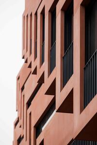 Rotes modernes Wohngebäude mit geometrischen Balkonen und schwarzen Geländern. Ansicht von unten, Fokus auf klare Linien und minimalistische Architektur.