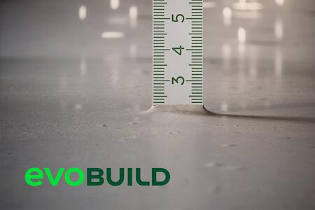 Nahaufnahme eines Zollstocks, der die Tiefe der Bodenoberfläche anzeigt. Unten links das grüne Logo von "evoBuild".