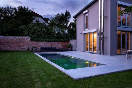 Modernes Wohnhaus mit beleuchtetem Pool und gepflegtem Garten bei Dämmerung.