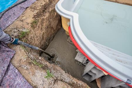 Ein Bauarbeiter in Schutzkleidung füllt Beton in eine Grube bei der Installation eines Pools.