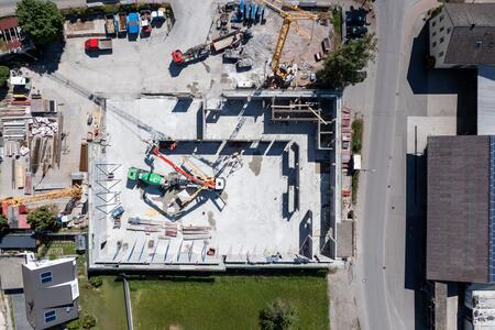 Baustelle mit Betonfundament und Baumaschinen, dargestellt aus der Vogelperspektive.