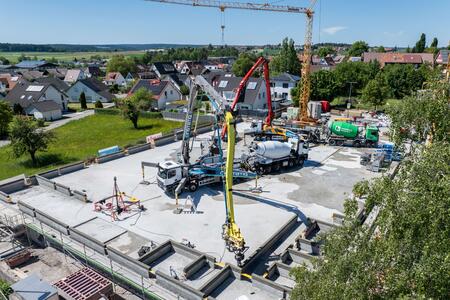 Eine 3D-Druck Baustelle mit Betonpumpen und Baukranen, umgeben von Wohnhäusern.