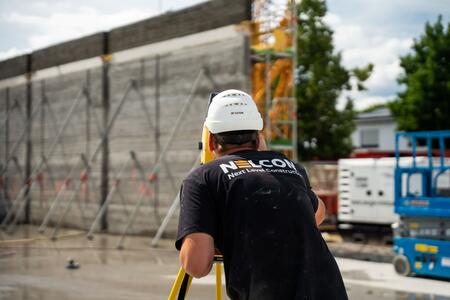 Ein Bauarbeiter mit Schutzhelm führt Vermessungsarbeiten auf einer Baustelle durch.