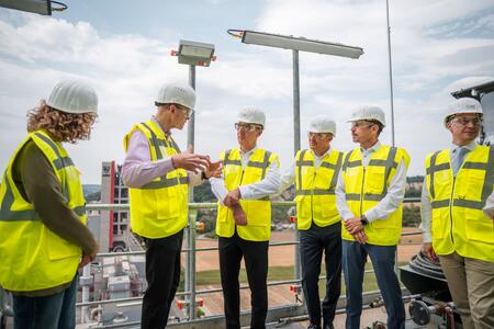 Personengruppe mit Sicherheitswesten und Helmen auf einer Baustelle bei einer Besprechung.