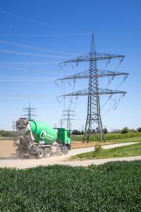 Ein grüner Betonmischer fährt auf einer Landstraße neben Strommasten durch eine ländliche Umgebung.