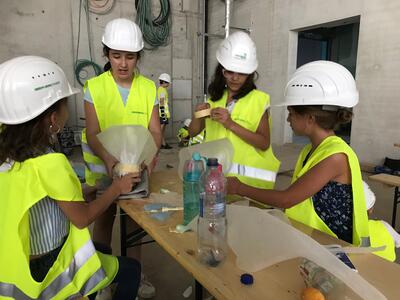 Kinder in PSA basteln gemeinsam an einem Tisch auf einer Baustelle.