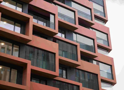 Moderne Wohngebäudefassade mit Balkonen aus rotem Sichtbeton.