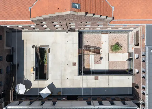 Drohnenaufnahme des zentralen Innenhofs des ehemaligen Bahnbetriebswerks in Heidelberg. Zu sehen sind sanierte Backsteinfassaden sowie neu angelegte, hell betonierte Bodenflächen und ein kleiner begrünter Bereich.